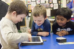 Three kids playing happy on an iPad at school 